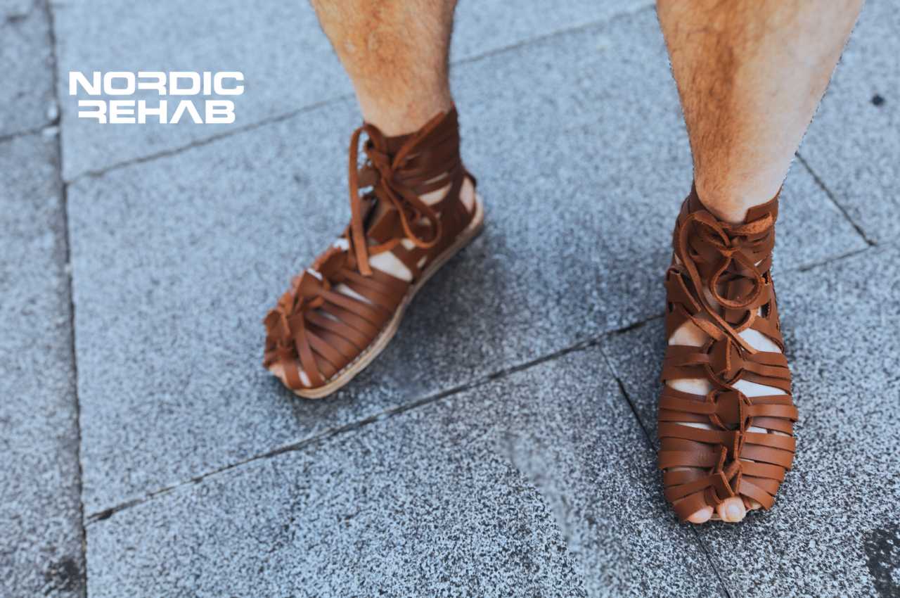 Närbild på en persons fötter i bruna sandaler inspirerade av romerska caligae, med Nordic Rehab-logotyp. Bilden används i en artikel om skoinläggens historia – från antikens Egypten och Rom till dagens moderna inlägg för komfort och stöd.