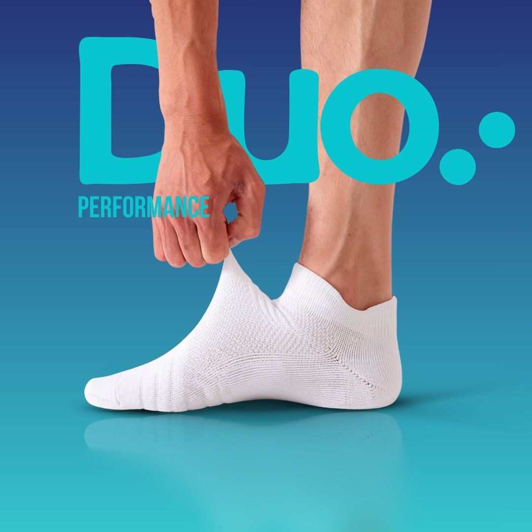 Närbild på en person som tar på sig Nordic Rehab Duo Performance – 5 zoners kompressionsstrumpa i vitt. En hand drar i tyget för att visa kompressionen i materialet. Strumpan har strategisk kompression som ökar blodcirkulationen, ger stöd för hålfot och ankel samt minskar trötthet i fötter vid träning, jobb och vardag.