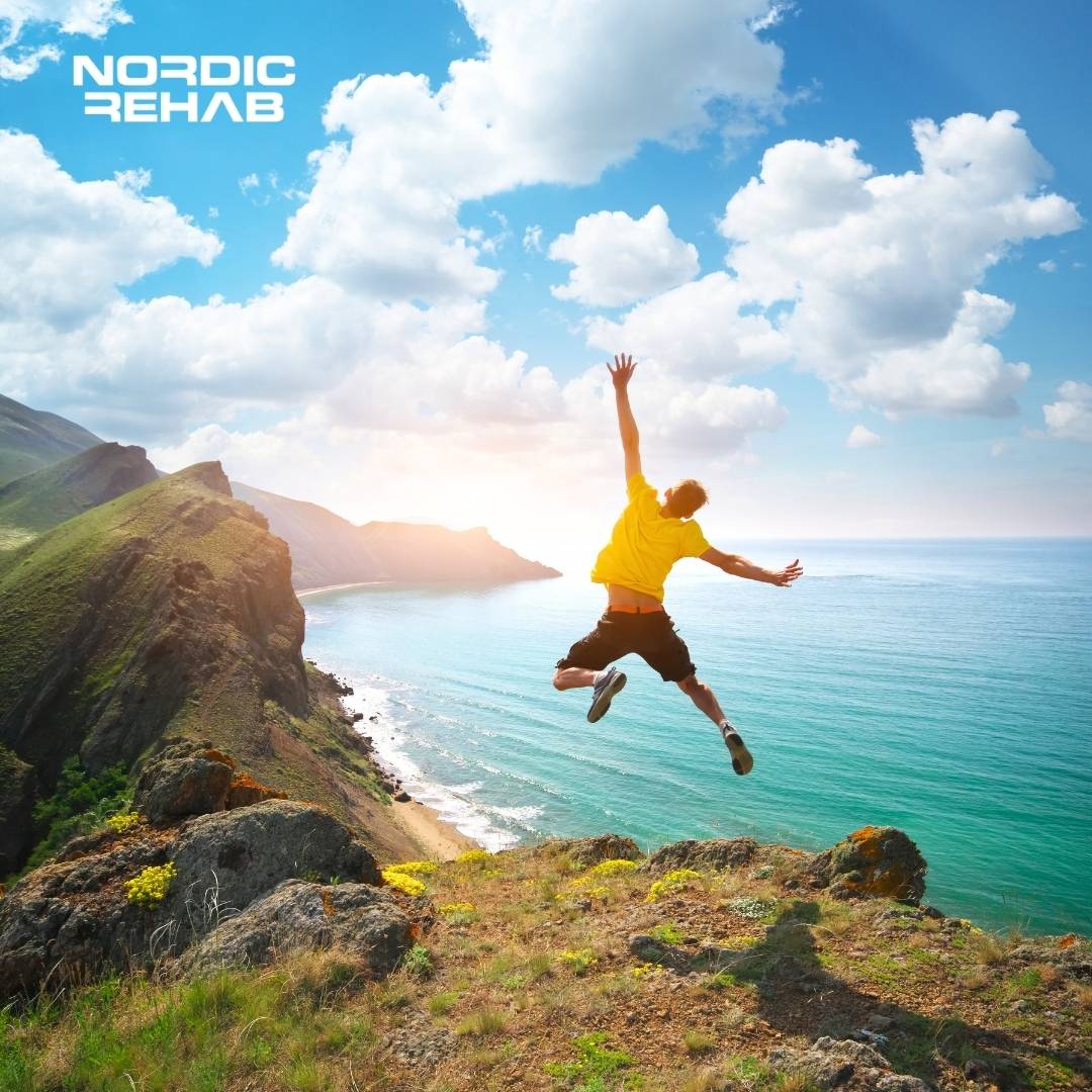 Bild från Nordic Rehab som visar en person som hoppar ut mot havet från en klippa en solig dag. Bilden symboliserar frihet, rörelseglädje och välmående – kärnvärden i Nordic Rehabs produkter för komfort och återhämtning.