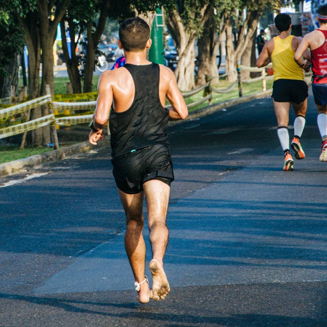 Bild från Nordic Rehab som visar en löpare som springer barfota på asfalt. Bilden speglar den naturliga rörelse och fotstyrka som NEO Sport barfotaskor erbjuder genom att främja korrekt löpteknik, markkontakt och starkare fötter.